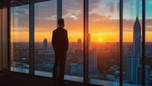 Business man looking out of office window at city sunset